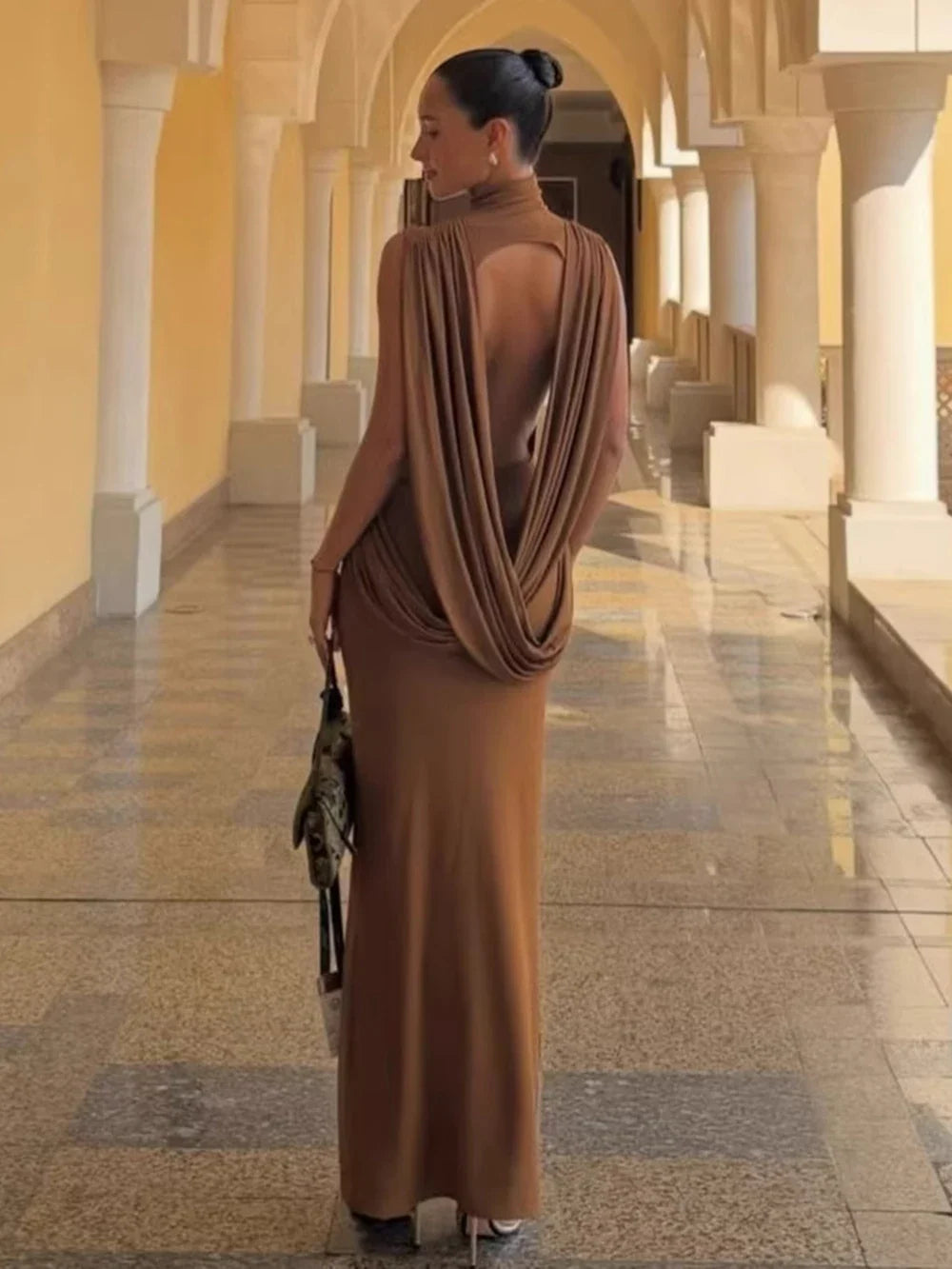Rear view of a woman wearing a brown draped open-back maxi dress.